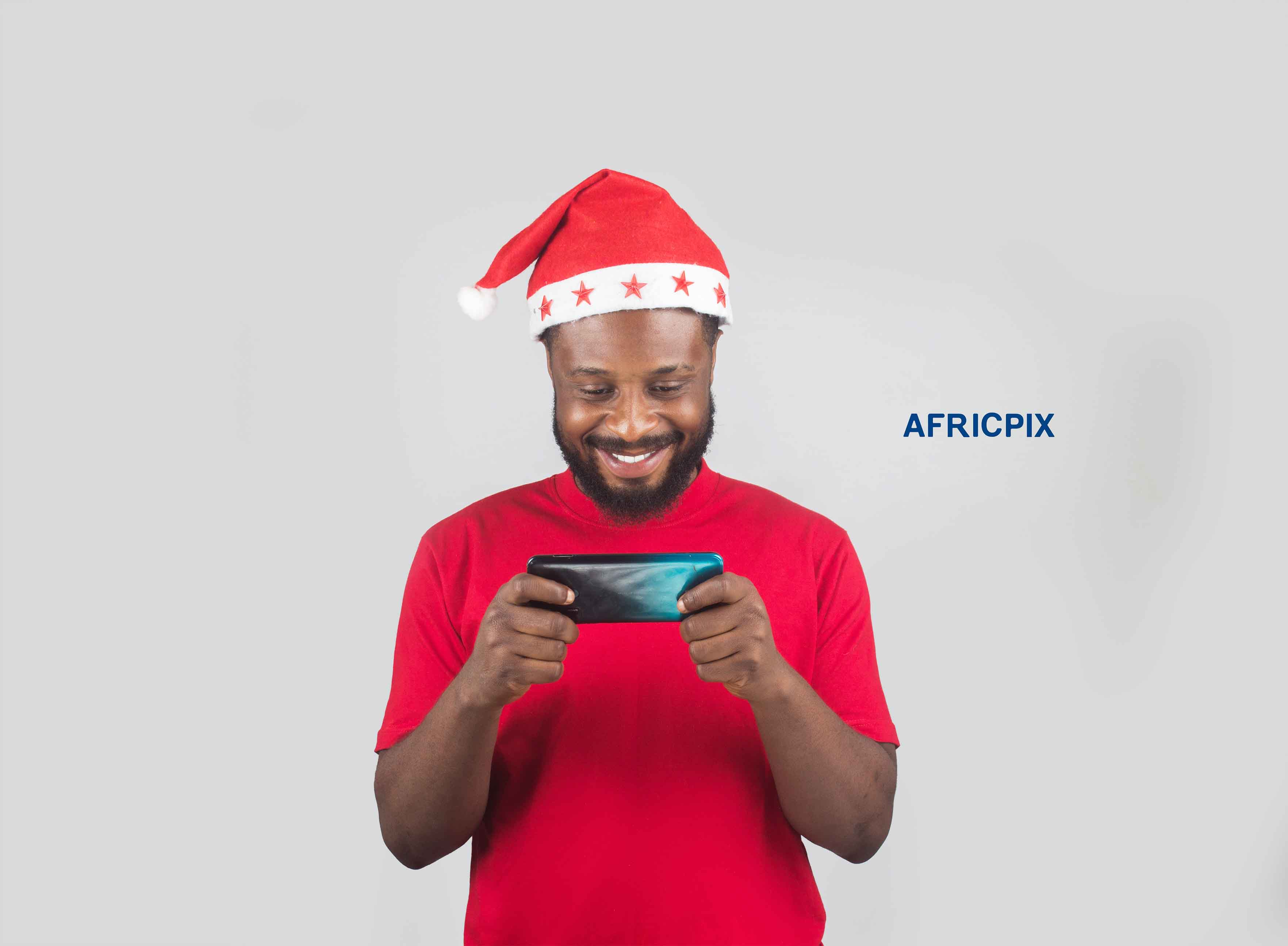 An African Nigerian man wearing a Christmas cap, holding a phone with both hands, looking Happy and excited